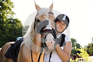 Young woman in horse riding suit and her beautiful pet outdoors on sunny day