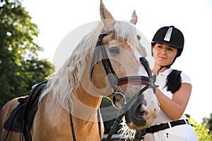 Young woman in horse riding suit and her beautiful pet outdoors on sunny day