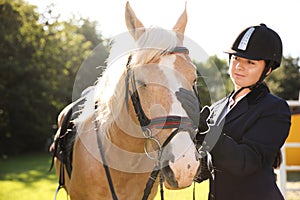 Young woman in horse riding suit and her beautiful pet outdoors on sunny day