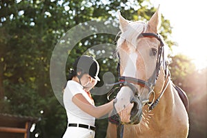 Young woman in horse riding suit and her beautiful pet outdoors on sunny day