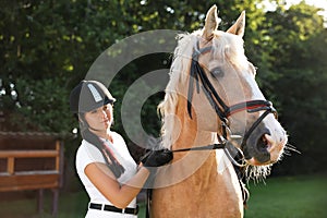 Young woman in horse riding suit and her beautiful pet outdoors on sunny day