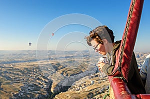 Young woman in hot air balloon basket, looking at balloons and beautiful landscape of Goreme, travel vacation, Cappadocia, Turkey