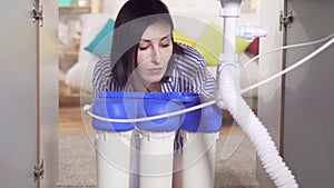 Young woman housewife looks under the sink and examines the water filter