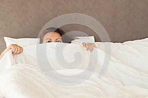 A young woman with huge frightened open eyes lying in bed and covers herself with the sheets and hides. Nightmares, insomnia, phob