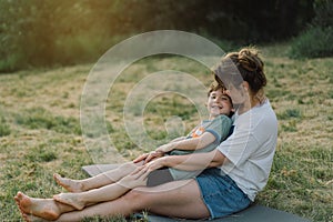 Young woman hugging her little son at sunny in the meadow.