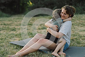 Young woman hugging her little son at sunny in the meadow.