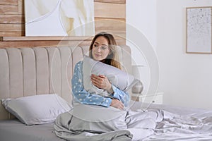 Young woman hugging pillow on bed with silky linens