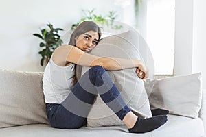 Young woman hugging pillow with depression and crying on sofa at home. Lonely millennial lady feeling stressed and hopeless,