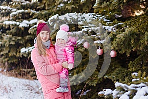 A young woman hugs little girl in a pink jumpsuit in winter