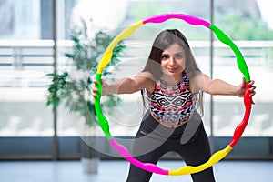 The young woman with hula loop in gym in health concept