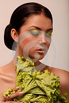 A young woman, I have green eyeshadow and lettuce leaves in my hands.