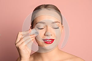 Young woman with ice cube on color background