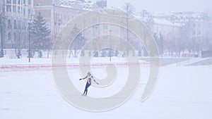 A young woman ice skating on the open rink outside alone. Heavy snowfall