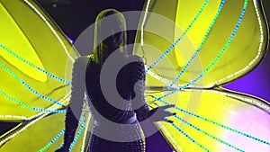 A young woman in the image of a butterfly with glowing and flashing wings poses against the background of dynamic