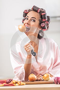 Young woman imitates onion biting with a knife in her hand and curlers in her hair