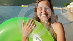 Young woman inflating an inflatable swimming ring on the shore at sunset. Essence of tourism, summertime bliss, oceanic