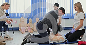 Young woman instructor helping to make first aid heart compressions with dummy during the group training indoors.