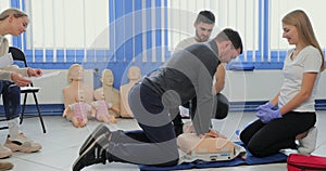 Young woman instructor helping to make first aid heart compressions with dummy during the group training indoors.