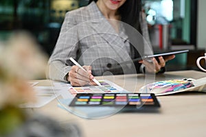 young woman interior designer working with color swatches and using digital tablet at her workplace