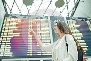 Young woman in international airport looking at the flight information board checking for flight