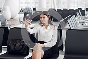 Young woman at international airport, making selfie with mobile phone and waiting for her flight.