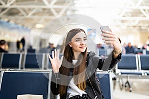 Young woman at international airport, making selfie with mobile phone and waiting for her flight. Female passenger at departure