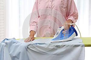 Young woman ironing clean shirt at home. Laundry day