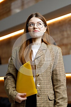 A young woman in a jacket with a yellow folder on the background of the office, purposefulness