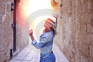 Young woman in jeans and hat dancing in sunset