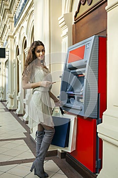 Young woman in jeans short using an automated teller machine