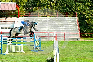 Young woman jockey ride beautiful white horse and jump over the crotch in equestrian sport.