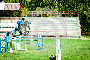 Young woman jockey ride beautiful white horse and jump over the crotch in equestrian sport.