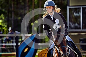 Young woman jockey in white black dress and black boots, takes part in equestrian competitions. Sunny summer day.