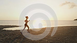 A young woman jogging at the beach on sunset. aerial drone shot, slow motion