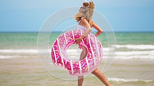 Young woman jogging with inflatable donut, with inflatable ring on the beach.