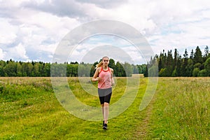 Young woman jogging in the meadow and listening to music on headphones