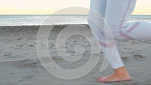 Young woman is jogging on the sand beach by the sea at sunrise in autumn, close-up legs side view.