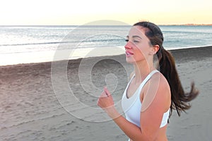 Young woman is jogging on the sand beach at sunrise in autumn, side view.