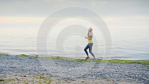 A young woman jogs along the shore of the sea or a lake, autumn, morning