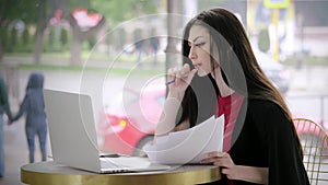 Young woman journalist write articles, takes notes on paper, works on a laptop against the background of city road traffic