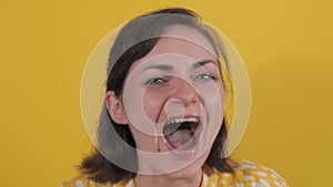 A young woman joyfully shouts and screams on a yellow background in slow motion