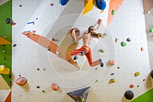 Young woman jumping on handhold in bouldering gym