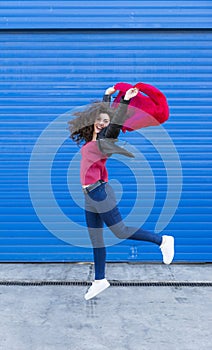 Young woman jumping and having fun with a red scarf over blue b