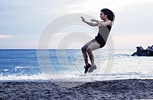 Young woman jumping high on the beach, working out