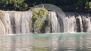 Young woman jumping in mountain lake from rope and splashing waterfall on background. Slow motion. Happy woman jumping