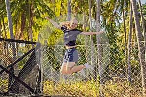 Young woman jumping on an outdoor trampoline, against the backdrop of palm trees