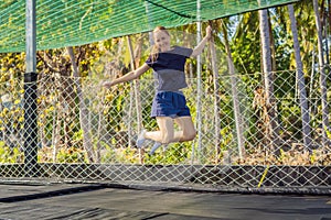 Young woman jumping on an outdoor trampoline, against the backdrop of palm trees