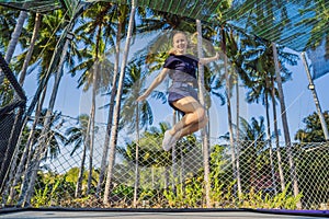 Young woman jumping on an outdoor trampoline, against the backdrop of palm trees