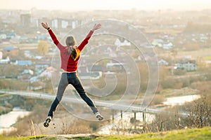 Young woman jumping with outstretched arms and legs outdoors on a distant city background. Relaxing, freedom and wellness concept