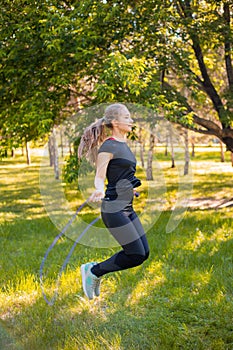 Young woman jumping rope on the lawn in a summer park. Jumping model. The concept of a healthy lifestyle and outdoor sports